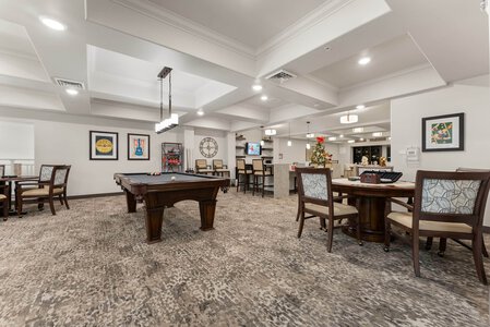 Spacious retirement community lounge with billiards table, comfortable chairs, and festive decor.