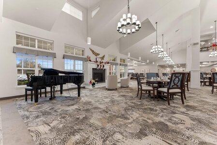 Spacious event hall decorated for holidays with grand piano, comfortable seating, and modern lighting fixtures.