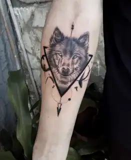Tatuajes 22 Retrato detallado de un lobo con ojos penetrantes, enmarcado por formas geométricas y elementos gráficos que aportan fuerza y modernidad al diseño.