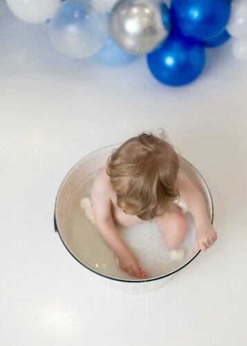 baby boy sitting in his milk bath tub during first birthday photoshoot in Little One Photography studio.
