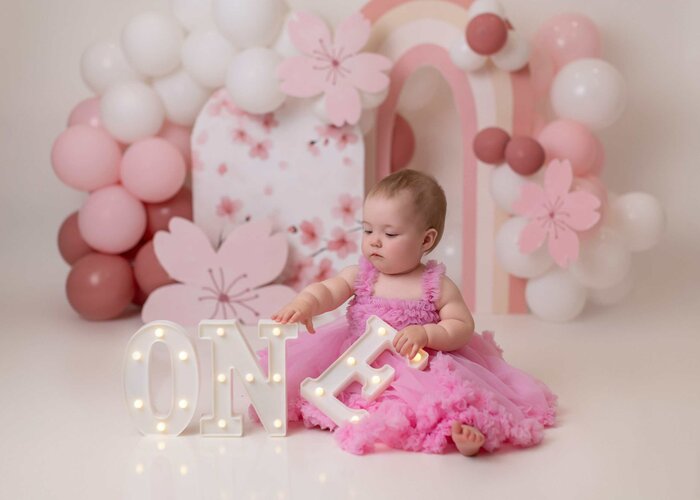 Edmonton cake smash photo featuring pink flowers, white ballons, and a dainty setup for a baby girl’s first birthday.