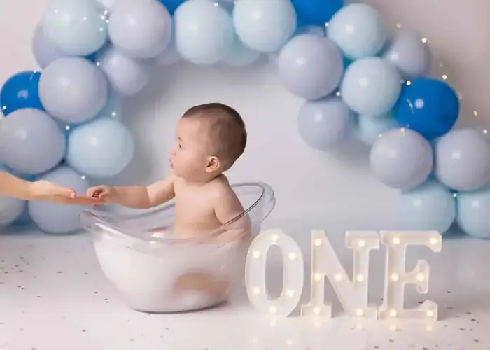 Light blue cake smash photo featuring a frosted cake, blue balloons, and baby boy milestone styling