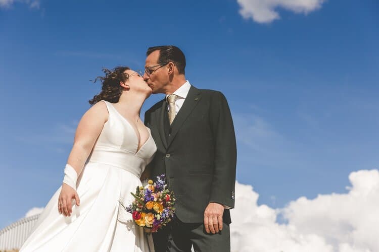 Trouwen bij Venster in Utrecht - Een bruidspaar kust elkaar onder een stralend blauwe lucht. Vastgelegd door trouwfotograaf Michella Kuijkhoven
