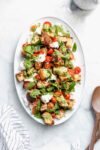pesto caprese panzanella salad drizzled with pesto on a serving platter