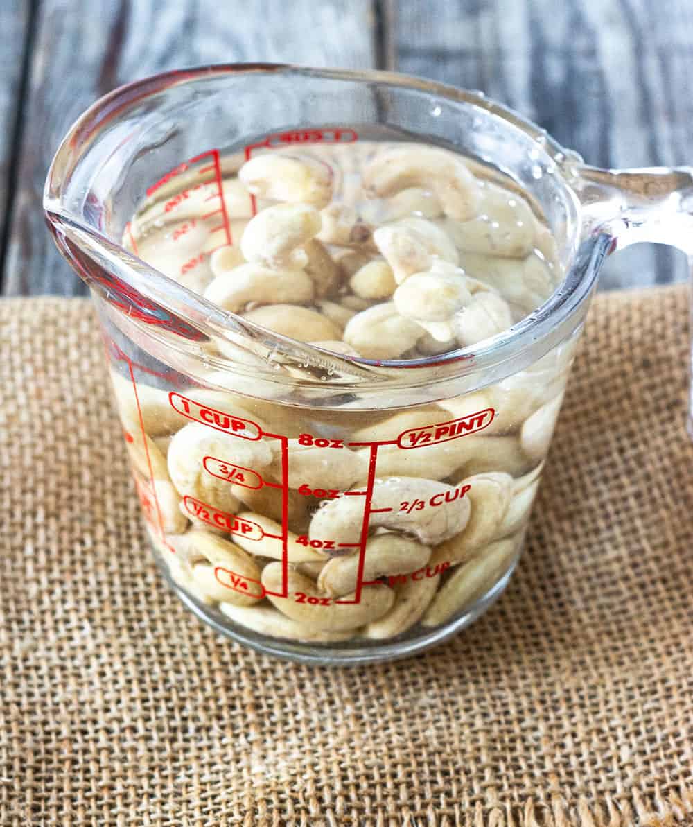 Soaked cashews in a measuring cup with water, place on a burlap napkin on a wooden board