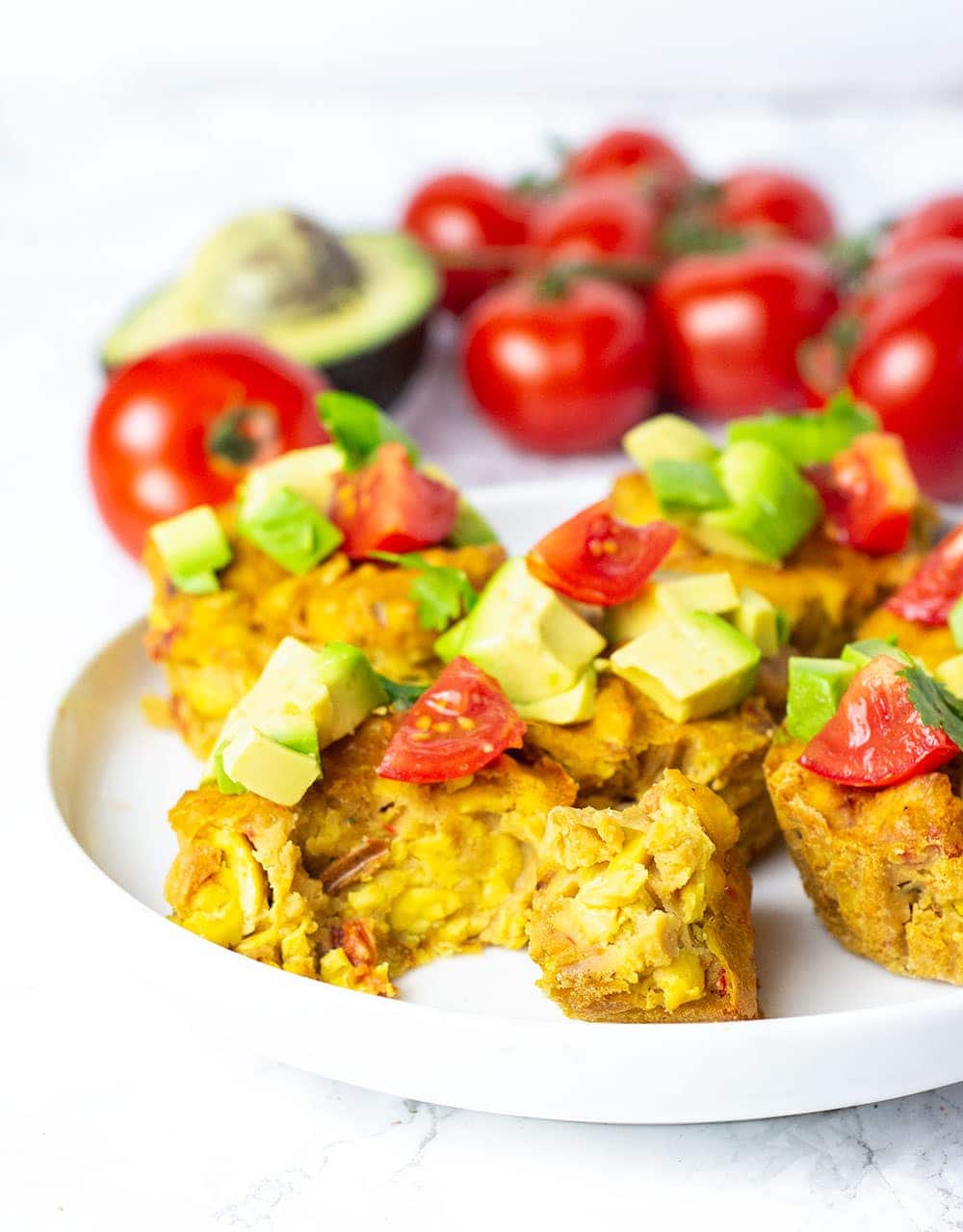 Straight on vegan ackee quiche recipe topped with avocado tomato and cilantro on a white plate with tomatoes on the vine