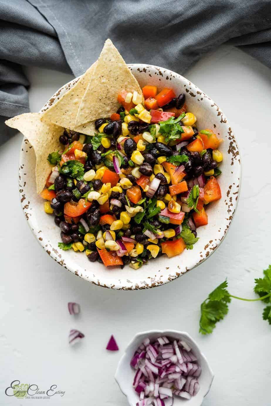 The salsa was serve with tortilla chips on the side there is chopped red onion in a white small bowl, cilantro and some chips on the side.