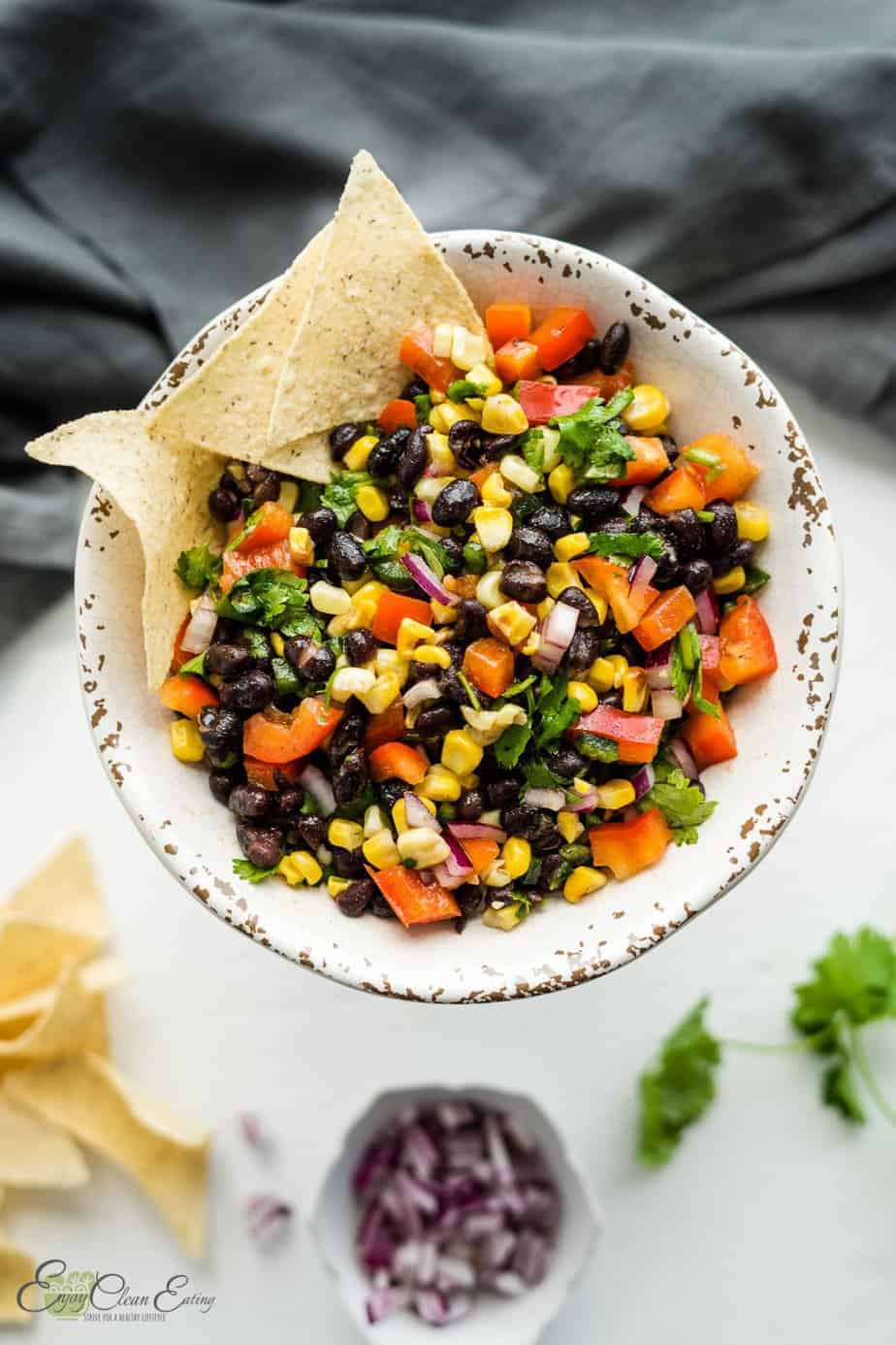 The salsa was serve with tortilla chips on the side there is chopped red onion in a white small bowl, cilantro and some chips on the side.