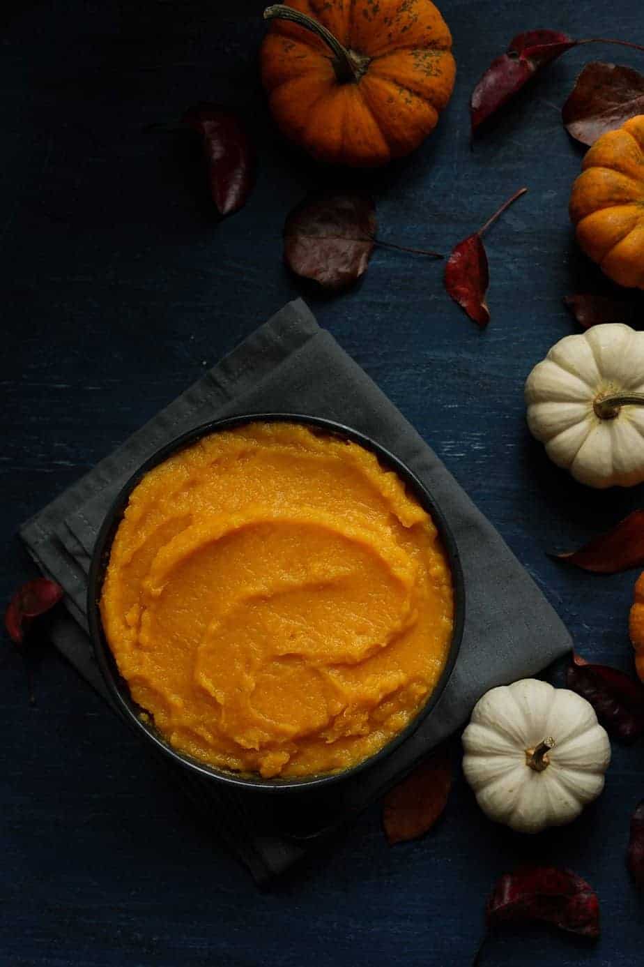 Fresh homemade pumpkin puree made using the instant pot pressure cooker. serve in a bowl to be store in the refrigerator around the bowl, there are pumpkins and leaves