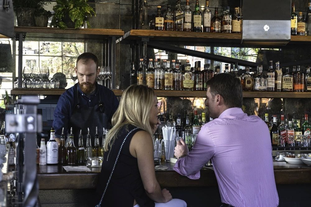 A well-dressed man and woman sit at a well-stocked and trendy bar in West Midtown, with a bartender behind the counter.