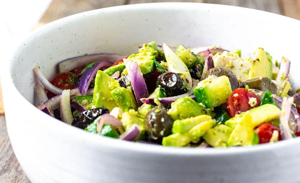 Close up vegan Greek salad with tomatoes, cucumber, red onions, avocado, olives in a white bowl