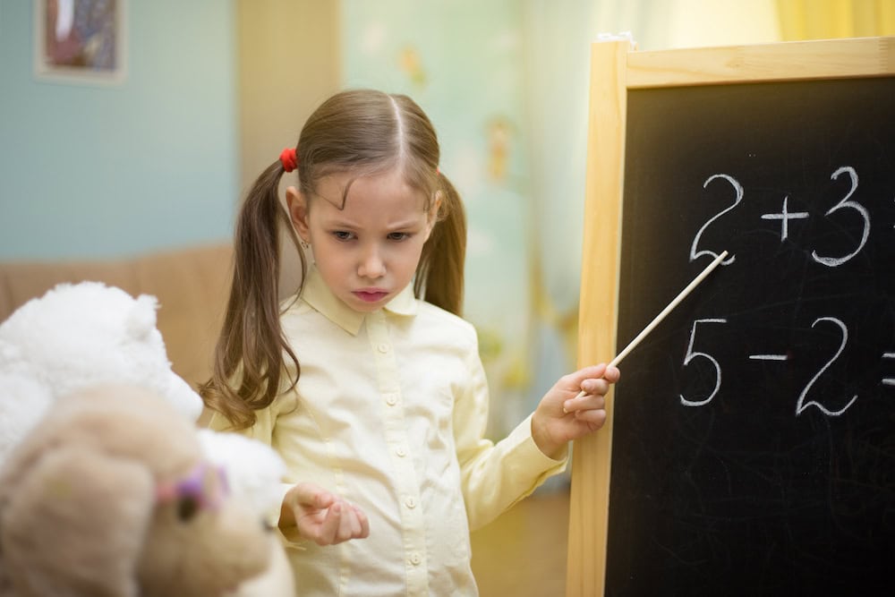 Photo of a young girl pretending to teach her stuffed animals how to add.
