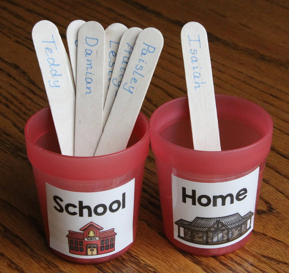Photo of two red cups, labeled "Home" and "School." Student name sticks are placed in the cups to indicate attendance.