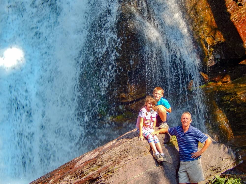 Father and kids sitting on a giant rock in front of a waterfall.