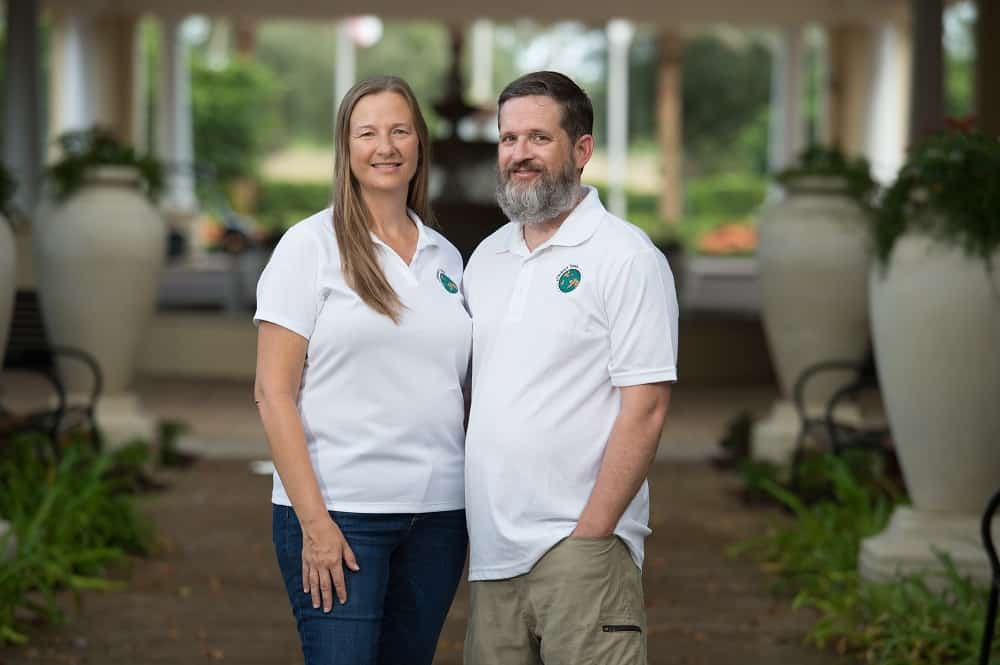A man with a beard and a woman with long harir standing closely together in similar white tee shirts