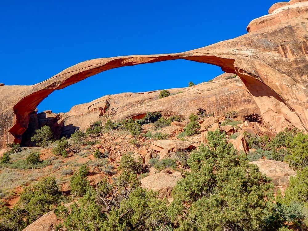 The rocks making an arch formation high up in the blue sky, with green shrubs on the ground