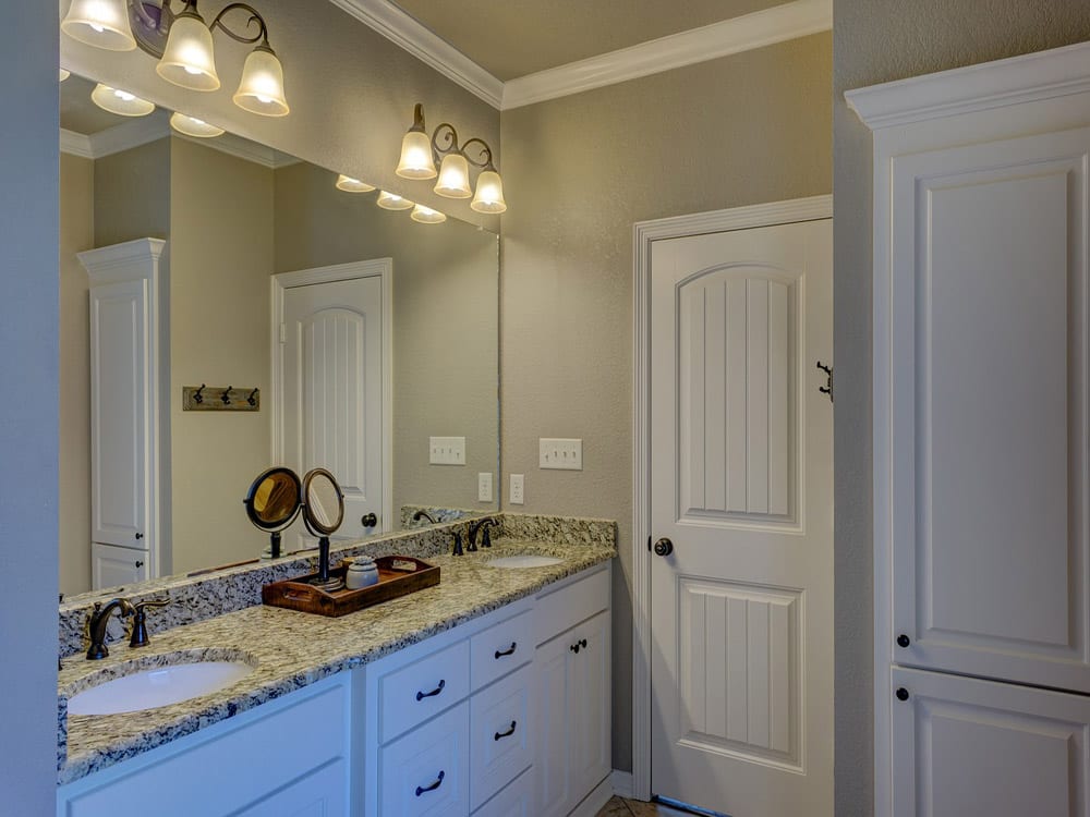 Bathroom remodeled with white cabinets, walls, and a granite countertop Dual sink remodel with granite countertops