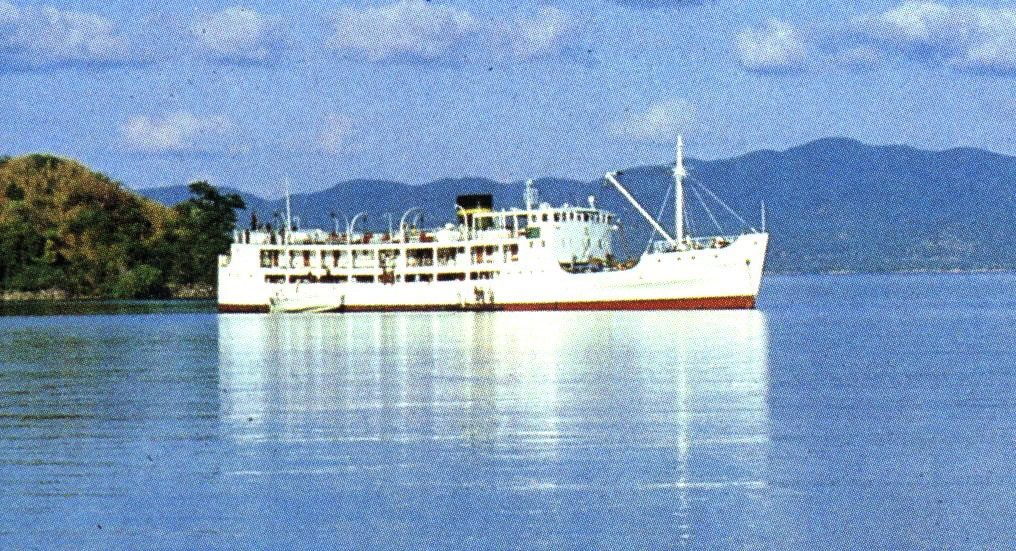 White steamer boat sits in calm harbor of blue water. Hills rise in the background behind the Itala ferry Malawi