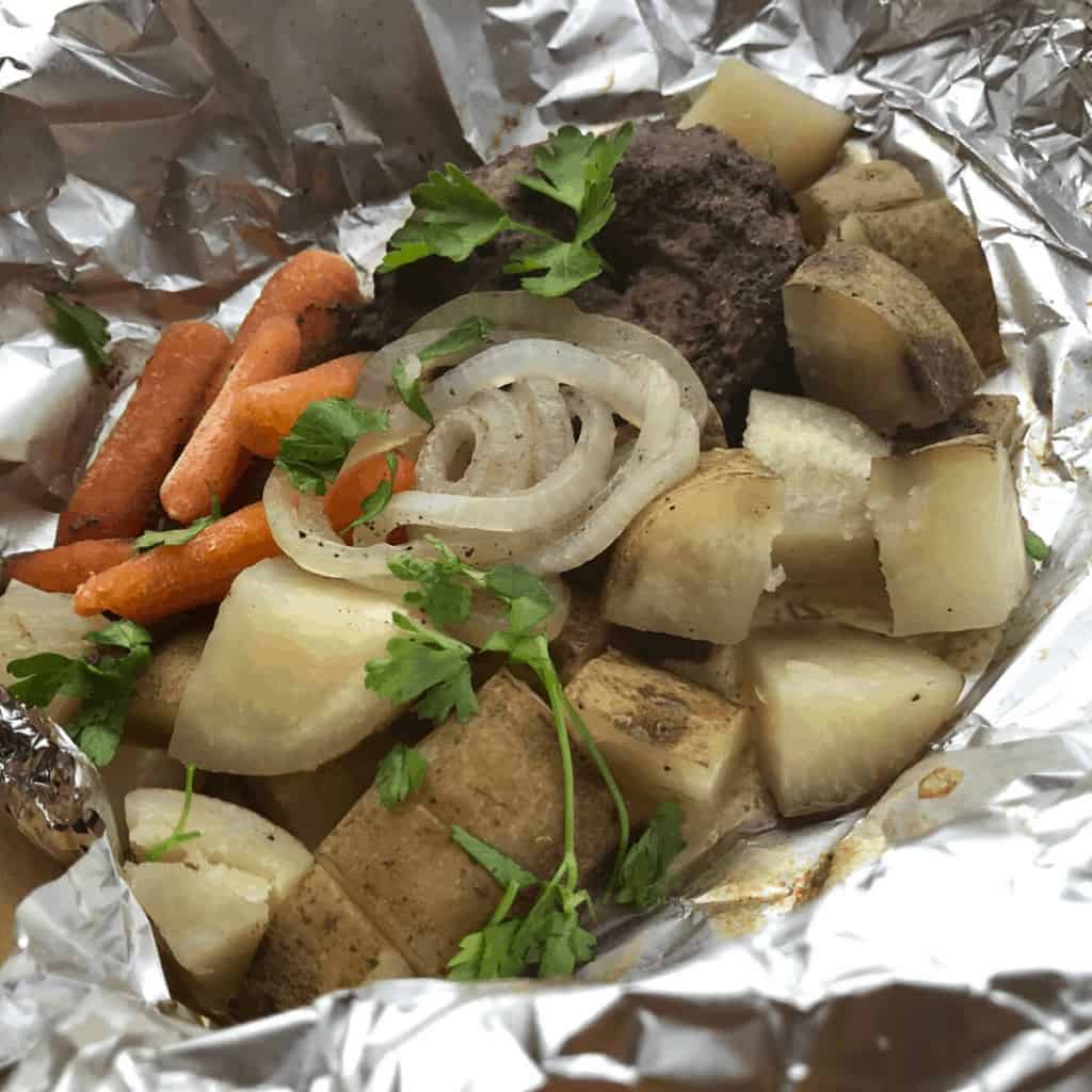 A hobo dinner consisting of hamburger, carrots, and potatoes on aluminum foil