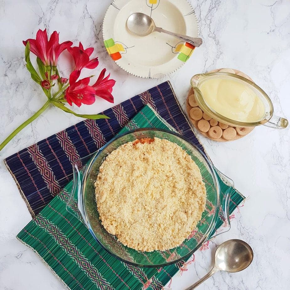Overhead shot of Gooseberry Crumble with a sauce jug full of dairy free custard