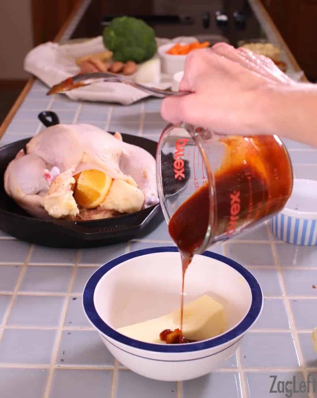 Adding BBQ sauce to the softened stick of butter in a bowl next to the raw stuffed chicken in a cast iron skillet