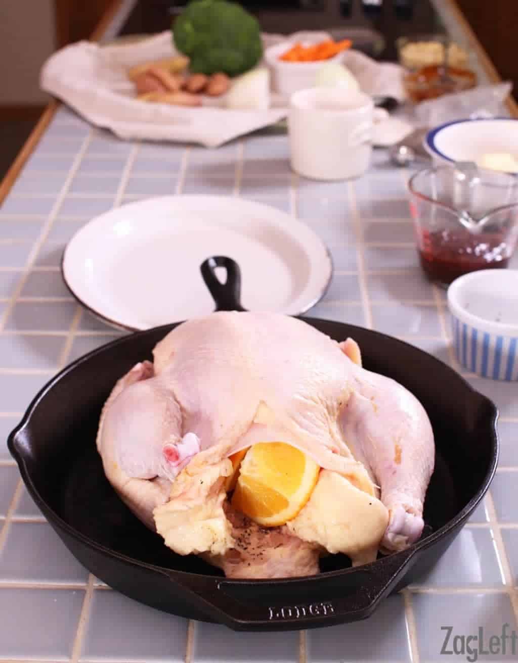 Raw chicken in a cast iron skillet stuffed with oranges and garlic