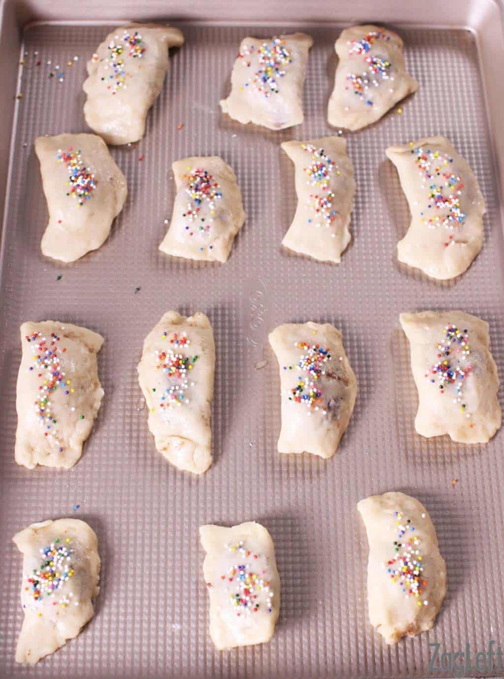 Fourteen Cuccidati's topped with rainbow sprinkles on a baking sheet