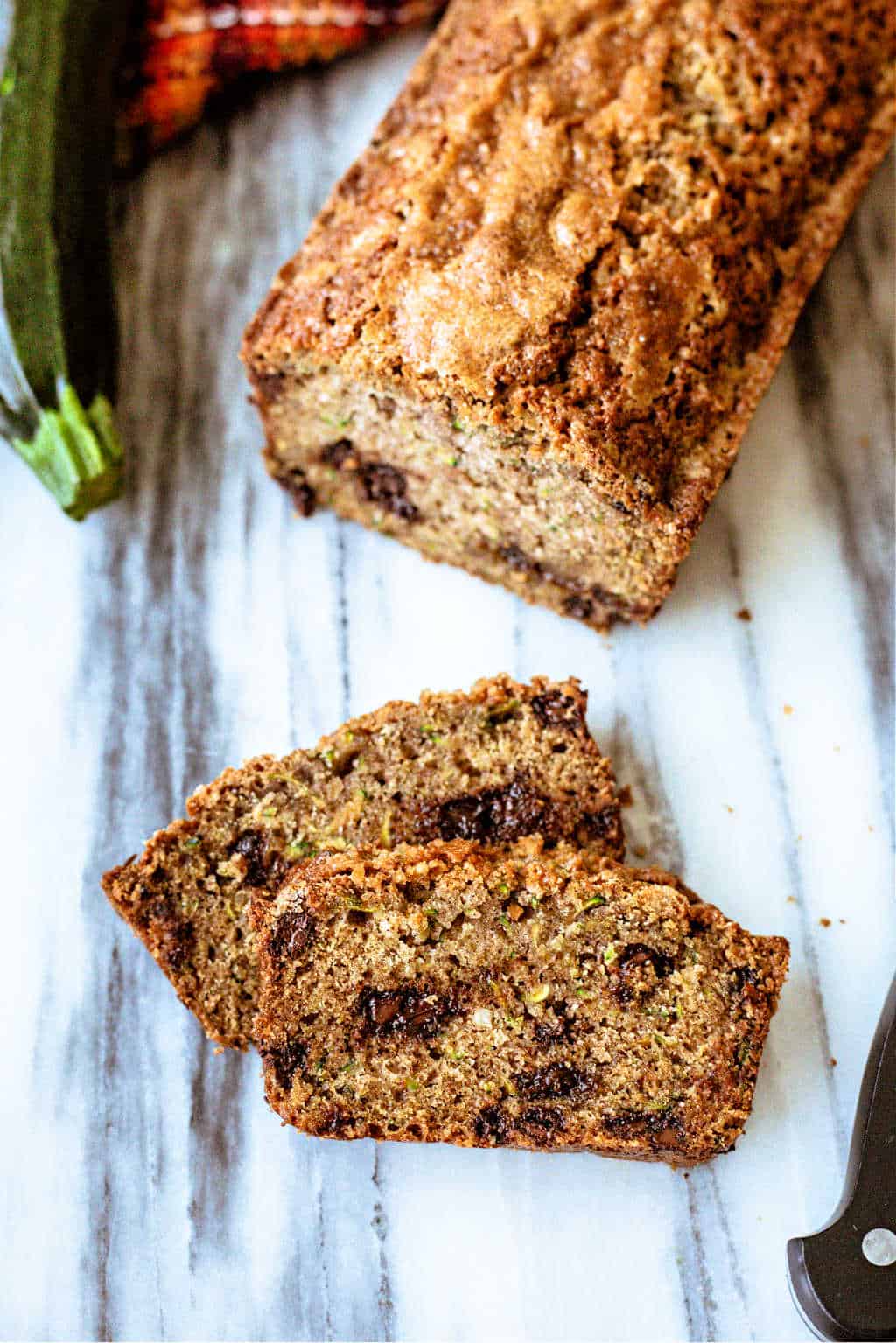 chocolate chip Zucchini Bread on a marble board with two cut slices and serrated knife