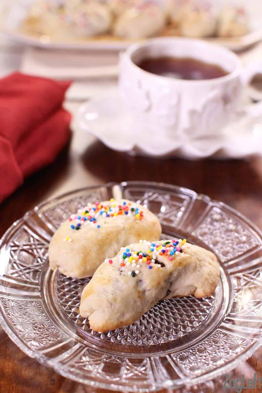 Two cuccidati's topped with rainbow sprinkles on a small plate next to a mug of coffee