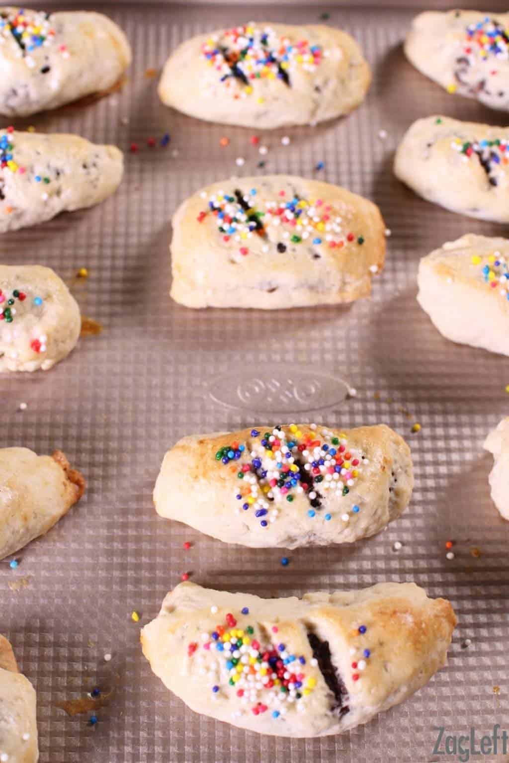 Cuccidati's topped with rainbow sprinkles on a baking sheet fresh out of the oven