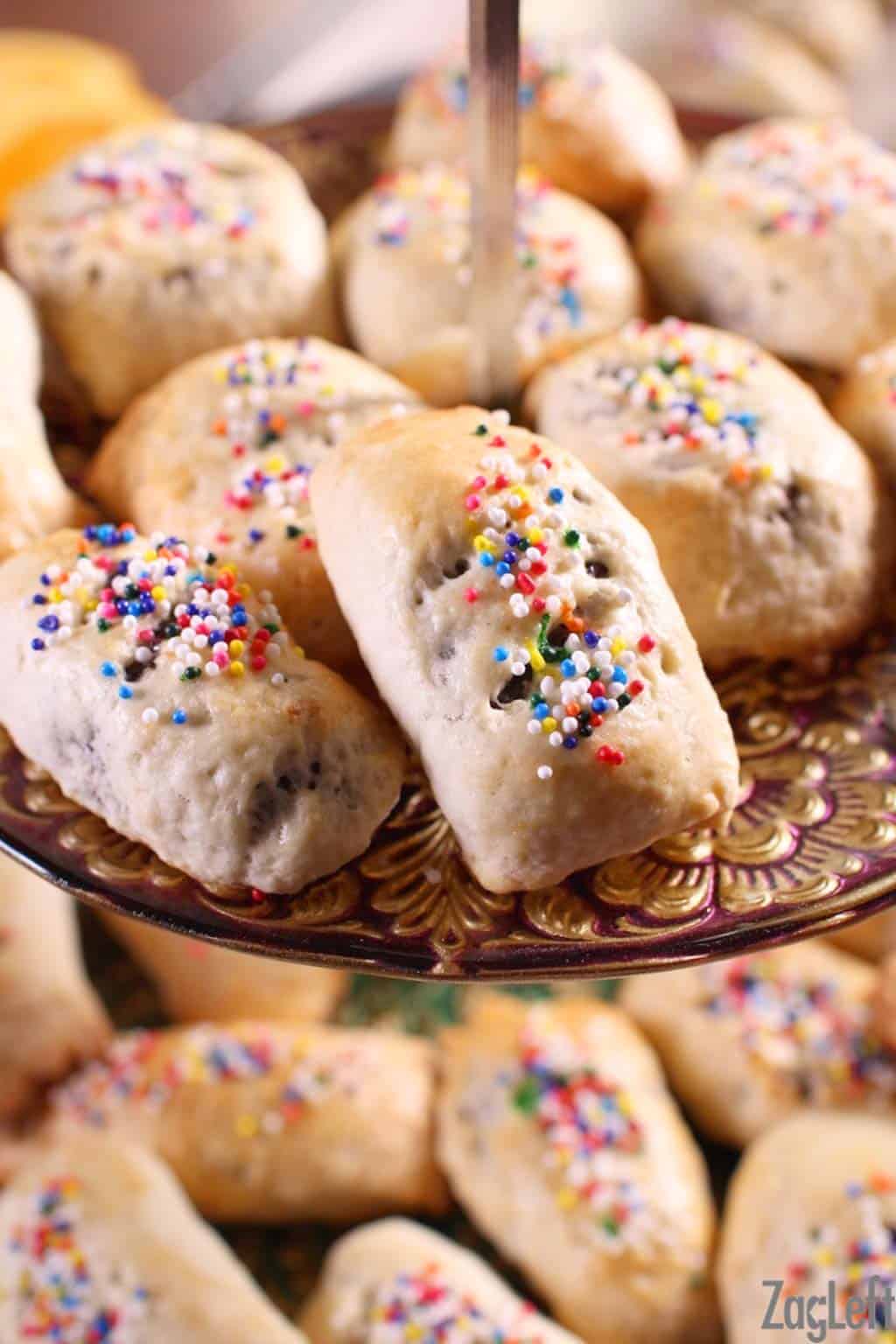 Cuccidati's topped with rainbow sprinkles on a dessert stand