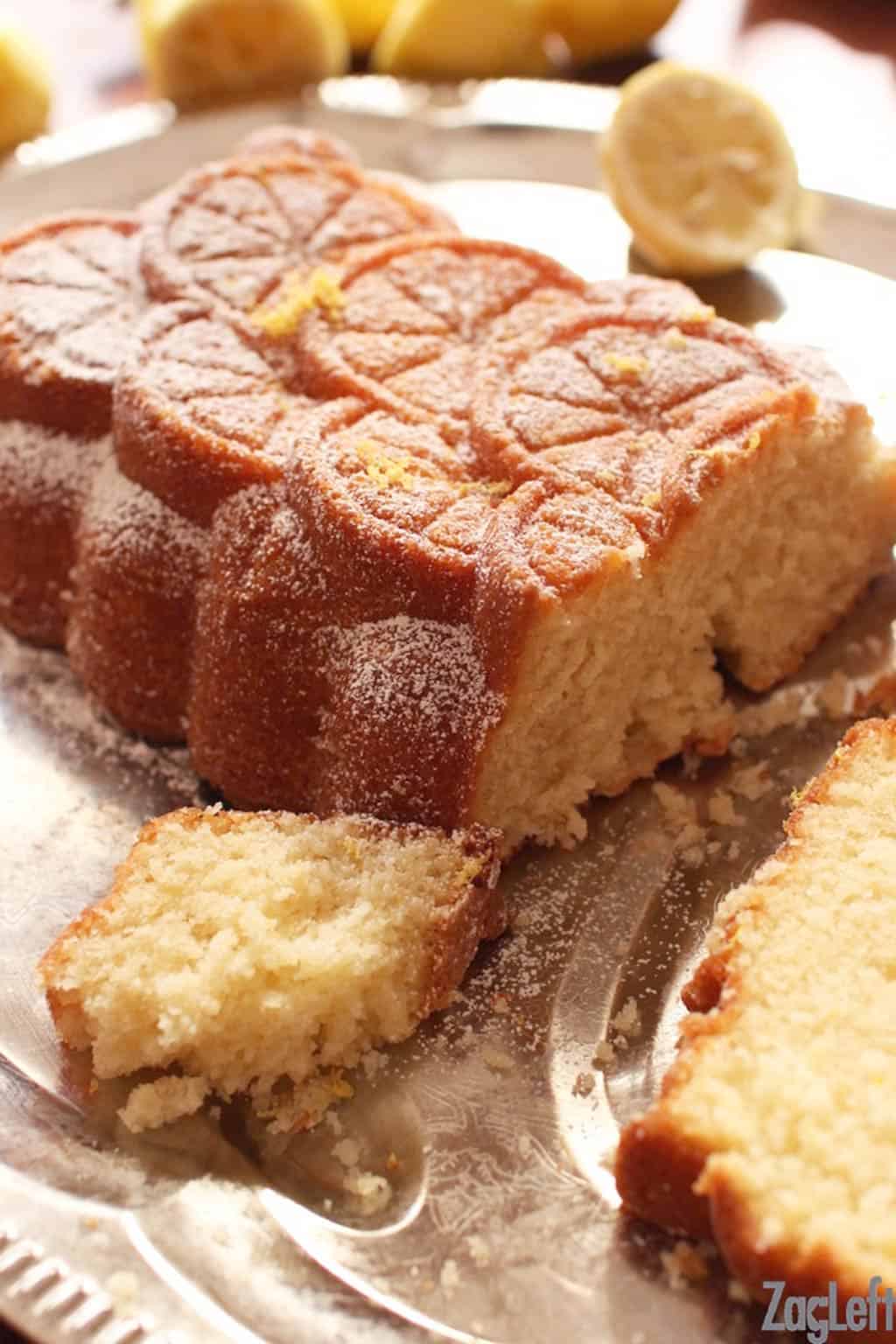 Sliced lemon cake dusted with powdered sugar and lemon zest on a metal tray