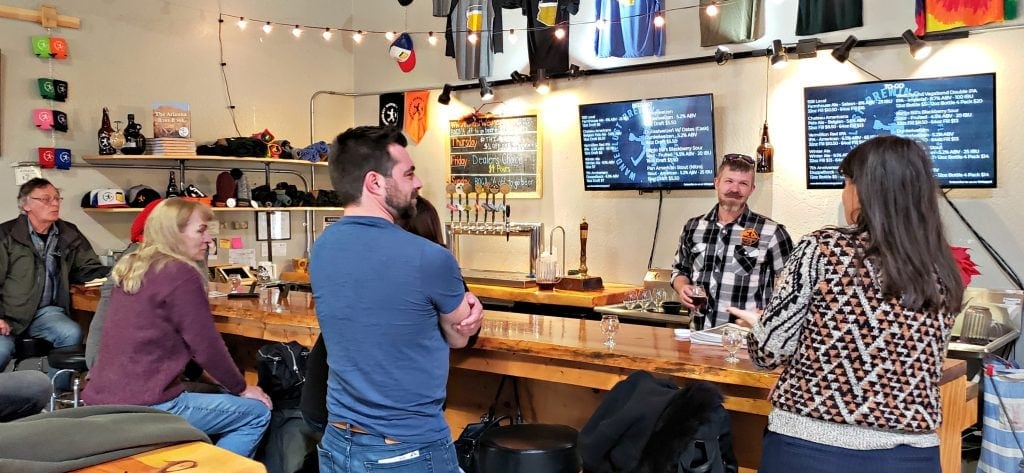 Customers sit around bar in warehouse area while a smiling Nathan Friedman, owner of the Flagstaff brewery, pours