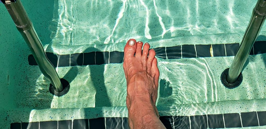 Woman's toe points to aquamarine water in clear swimming pool