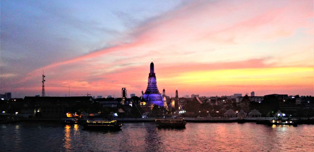 brilliant sun set over a Thai temple is reflected from the river in front of the rooftop bar in Bangkok