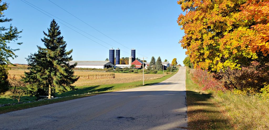 farm with 3 tall silos on top of hill with county road stretching to it on the Wisconsin pilgrimage