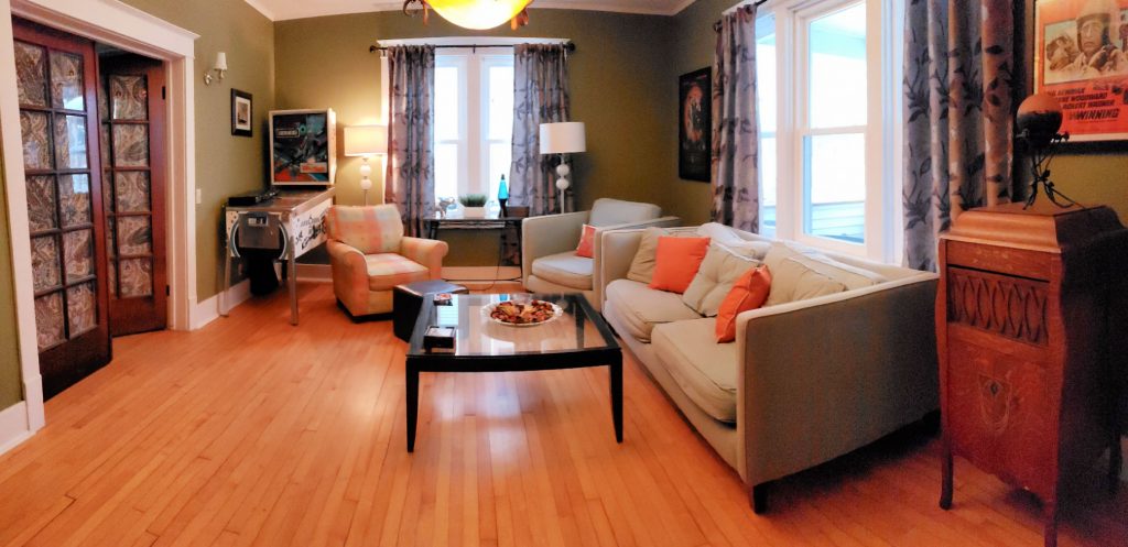 sitting room in this Elkhart Lake lodging has eclectic design including midcentury modern couches with orange pillow, hardwood floor, original dark woodwork, modern green walls