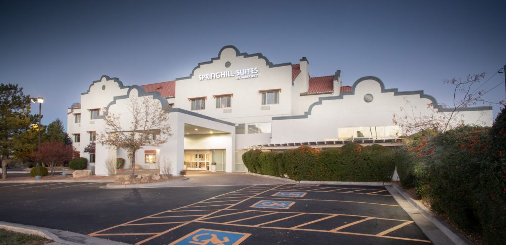 Exterior of 3-story hotel in Prescott AZ: white, adobe-style walls with Santa Fe-style trim and red tile roof. Clean facade and parking lot show this is one of the top lodging in Prescott
