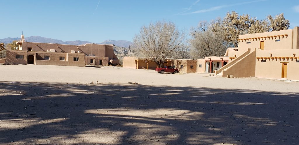 Large plaza in foreground withtwo-story pueblo buildings of adobe surrounding.