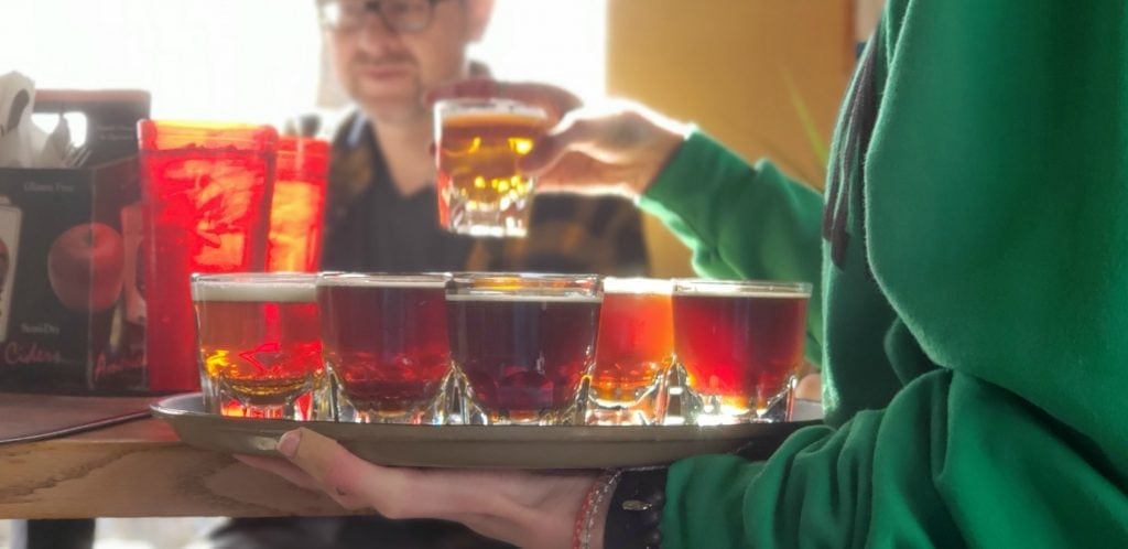 close up of server holding tray of Flagstaff craft beers - man smiles in back