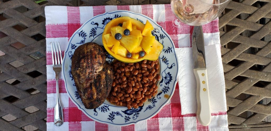 Plate of smoked chicken breast, brown beans and half a papaya filled with pineapple chunks, blueberries and chunked papaya