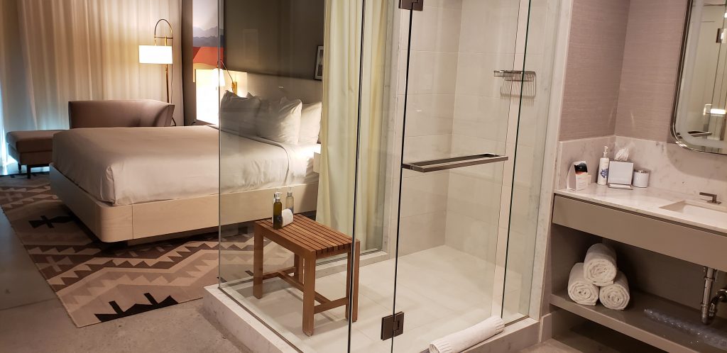 Stand alone glass shower has teak bench - can see king-sized bed through the glass enclosure