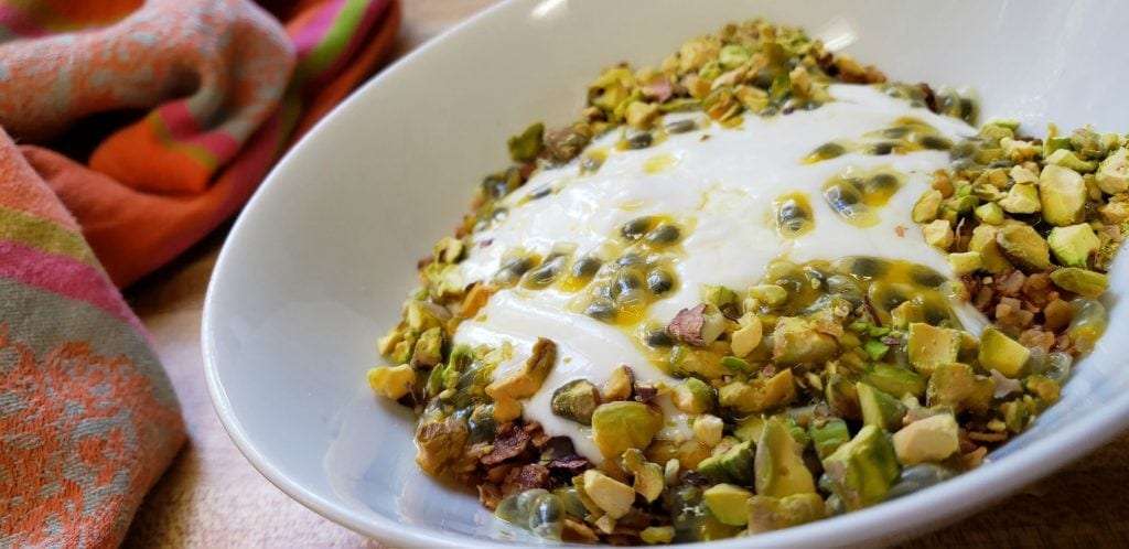 white bowl filled with yogurt, dribbled with green passion fruit seeds and juice, sprinckled with chopped pistachios