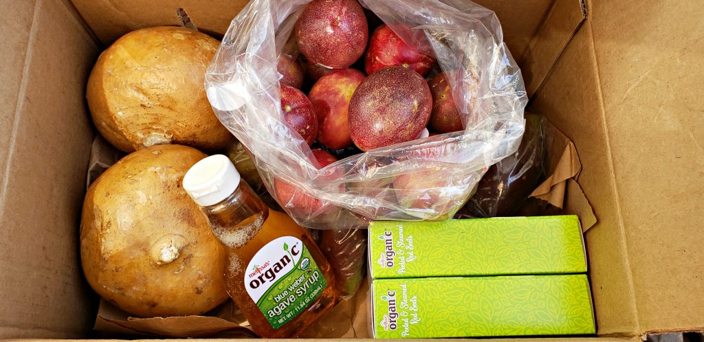 produce box open and looking into see passion fruit, jicama and bottle of blue agave syrup