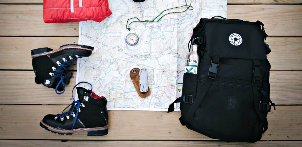 still life with black backpack, black boots laid out on map with compass shows Best Backpack for Air Travel