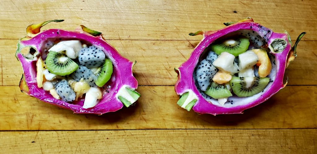 dragon fruit sliced in two, hollowed out and the fushia pink rind filled with cubes of white fruit, sliced green kiwi and chunks of pink papaya and cream-colored cherimoya