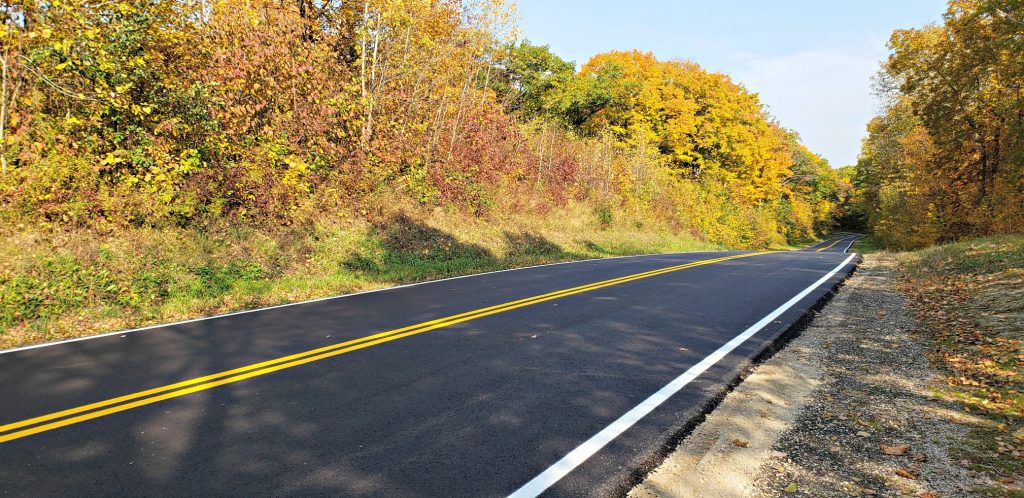 Fresh yellow and white road stripes on black asphalt road makes a pleasant picture as it rolls through thich forest decked in fall colors