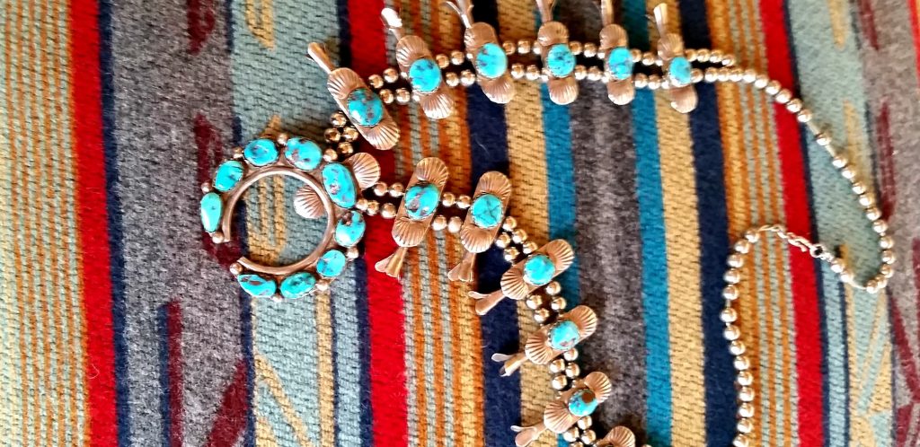 Large squash blossom necklace with snow white turquoise lays on colorful woven blanket is sample of Native jewelry one of the hings to see in Flagstaff
