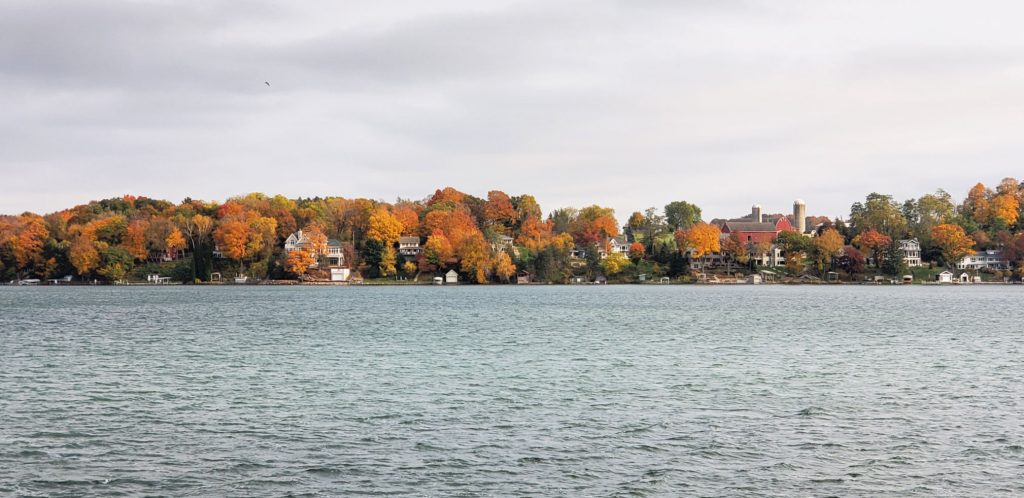 big lake with a little chop from the wind is in forground. Woods and red barn with tall silo stand on the opposite shore on this part of the WI Way pilgrimage