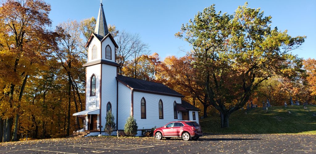 St Matthias Church: a white clapboard church with tall steeple has a backdrop of forest in fall colors